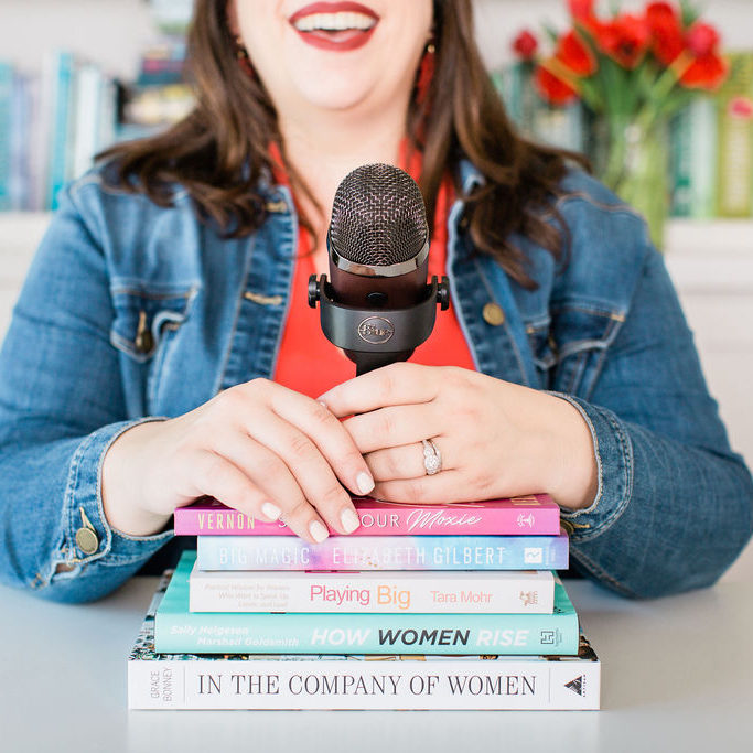 Renee Dalo with podcast mic on a stack of books #podcast #reneedalo